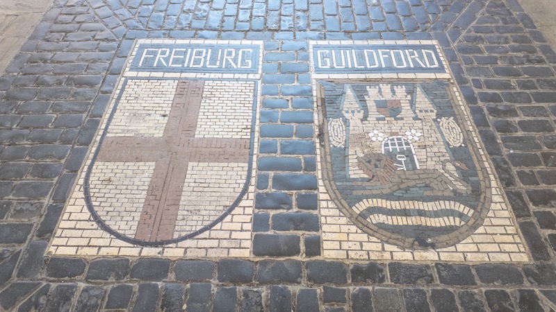 Circular mosaic crests of twin towns Freiburg and Guildford set into granite paving setts