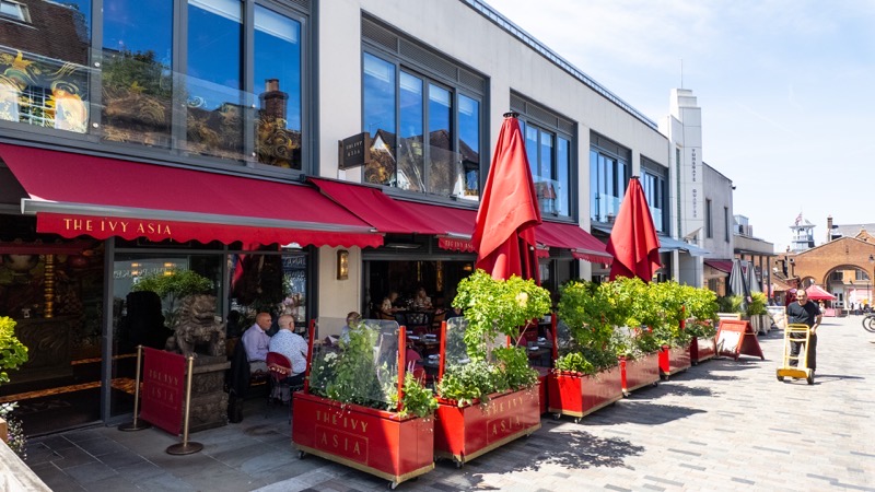 Diners at outdoor terrace tables outside The Ivy Asia restaurant on a paved courtyard