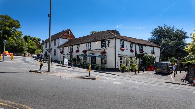 A traditional white-rendered corner pub with hanging baskets on a Guildford street